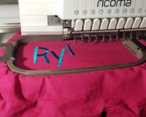 Commercial embroidery machine stitching custom blue name lettering onto pink fabric