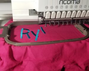 Commercial embroidery machine stitching custom blue name lettering onto pink fabric